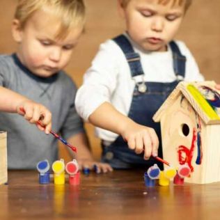2-børn-koncentreret-om-at-male-hver-deres-fuglehus-i-træ
